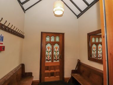 An entryway with wooden benches on either side a wooden door with stained glass panels and a mirror on the wall at Old School Muncaster House in Ravenglass near Holmrook