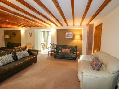 A living room with three sofas two striped cushions a wooden chair a floor lamp exposed wooden ceiling beams and a wall clock at Old School Muncaster House Ravenglass near Holmrook