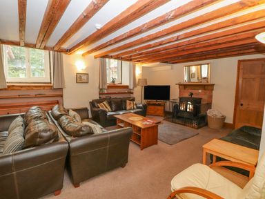 A living room with brown leather sofas a wooden coffee table a fireplace and a television at Old School Muncaster House Ravenglass near Holmrook