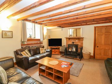 A living room with leather sofas a coffee table a television and a fireplace at Old School Muncaster House Ravenglass near Holmrook
