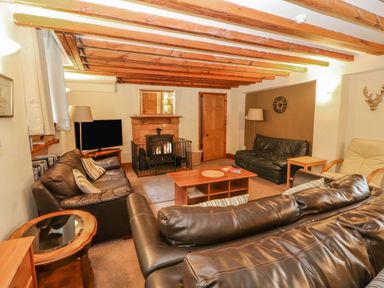 A living room with leather sofas a coffee table a fireplace and exposed wooden beams at Old School Muncaster House Ravenglass near Holmrook