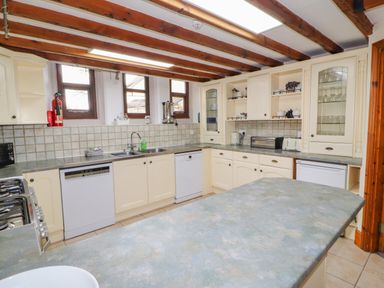 A kitchen with cream cabinets a countertop dishwasher sink stove and wooden ceiling beams at Old School Muncaster House Ravenglass near Holmrook