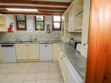 A kitchen with cream cabinets a tiled floor a countertop with toaster kettle and bread box and three small windows above the sink at Old School Muncaster House Ravenglass near Holmrook