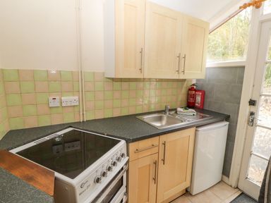 A kitchen with a stove, sink, cabinets, small refrigerator, fire extinguisher, and a door with window panels at Old School Muncaster House in Ravenglass near Holmrook