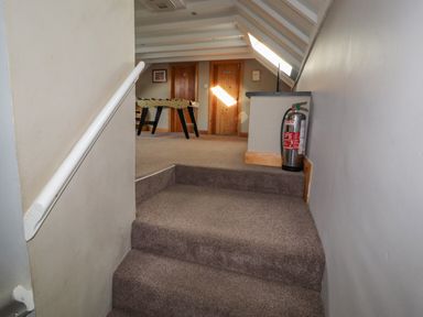 A carpeted hallway with two wooden doors a foosball table and a fire extinguisher at Old School Muncaster House Ravenglass near Holmrook