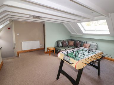 A game room with a foosball table a sectional sofa with pillows a small wooden table and a skylight window at Old School Muncaster House Ravenglass near Holmrook