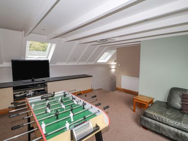 A game room with a foosball table, television, small wooden table, and leather sofa at Old School Muncaster House Ravenglass near Holmrook