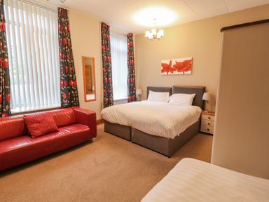 A bedroom with a double bed bedside tables a red sofa curtain and a wall mirror at Old School Muncaster House Ravenglass near Holmrook