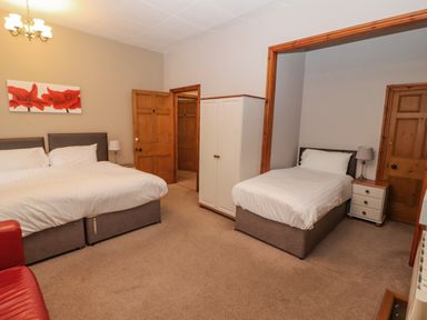 A bedroom with a double bed a single bed a wardrobe bedside tables and wooden doors at Old School Muncaster House Ravenglass near Holmrook