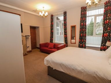 A bedroom with a bed a red sofa two windows with floral curtains and a door at Old School Muncaster House Ravenglass near Holmrook