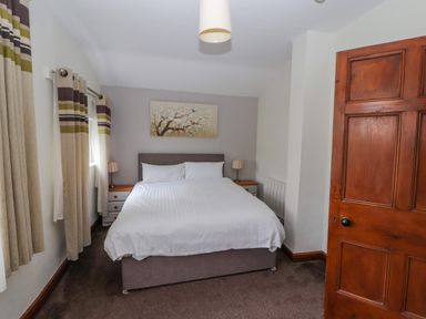 A bedroom with a double bed bedside tables curtains and a wooden door at Old School Muncaster House Ravenglass near Holmrook