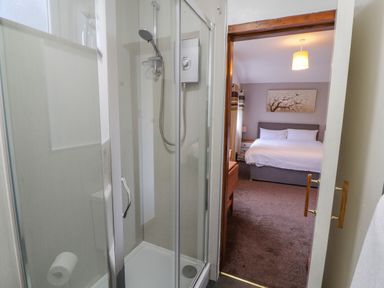 A shower enclosure with a glass door and a bedroom visible through an open door at Old School Muncaster House Ravenglass near Holmrook