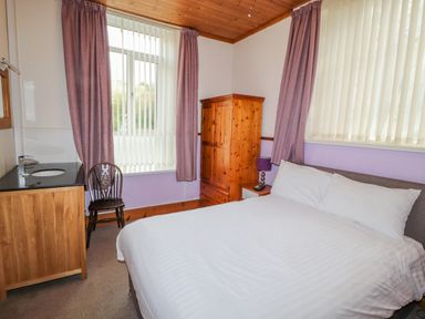 A bedroom with a double bed a wooden wardrobe a chair and a sink at Old School Muncaster House Ravenglass near Holmrook