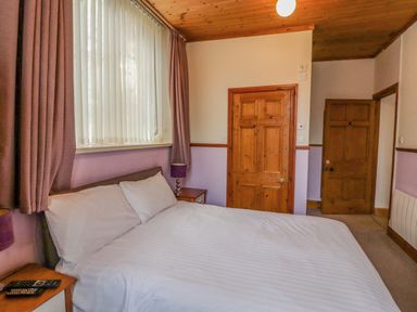 A bedroom with a double bed white bedding wooden furniture and two wooden doors at Old School Muncaster House Ravenglass near Holmrook