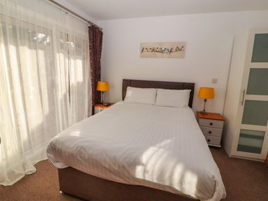 A bedroom with a double bed two bedside tables yellow lamps a wardrobe and sheer curtains at Old School Muncaster House Ravenglass near Holmrook