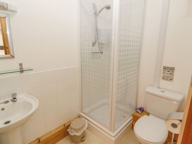 A bathroom with a shower cubicle toilet sink mirror and waste bin at Old School Muncaster House Ravenglass near Holmrook