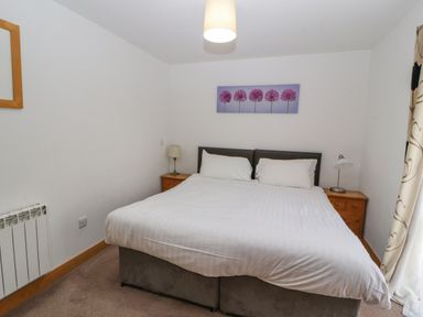 A bedroom with a double bed two bedside tables with lamps a painting of trees a curtain and a mirror at Old School Muncaster House Ravenglass near Holmrook