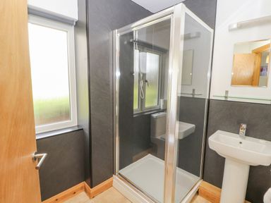 A bathroom with a glass shower enclosure a white pedestal sink and a frosted window at Old School Muncaster House in Ravenglass near Holmrook