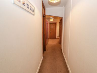 A narrow hallway with beige walls and carpet leading to a wooden door labeled with the number five at Old School Muncaster House Ravenglass near Holmrook