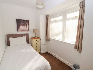 A small bedroom with a single bed a bedside table with a lamp a window with curtains and a wall picture at Old School Muncaster House Ravenglass near Holmrook