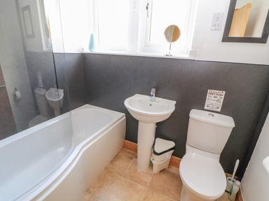 A bathroom with a bathtub, pedestal sink, toilet, small trash bin, and a mirror at Old School Muncaster House Ravenglass near Holmrook