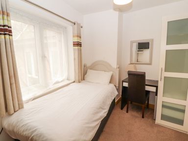 A small bedroom with a single bed next to a window and a desk with a chair and lamp at Old School Muncaster House Ravenglass near Holmrook