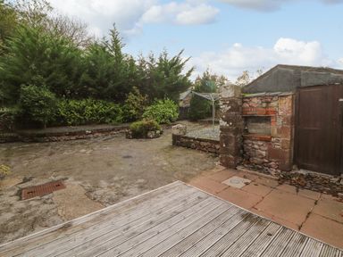 An outdoor space with wooden decking stone paving an old stone and brick structure and green trees in the background at Old School Muncaster House Ravenglass near Holmrook
