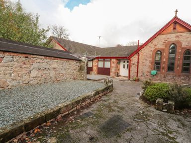 An outdoor courtyard area with stone walls a clothesline and a building with arched windows at Old School Muncaster House in Ravenglass near Holmrook