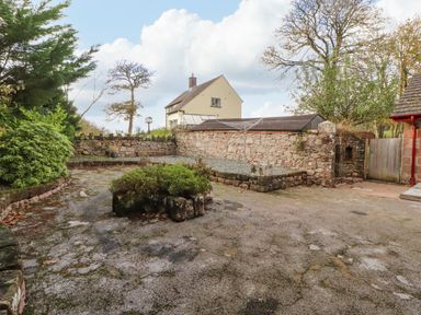 An outdoor courtyard with stone walls, shrubs, a rotary clothesline, and a house in the background at Old School Muncaster House Ravenglass near Holmrook