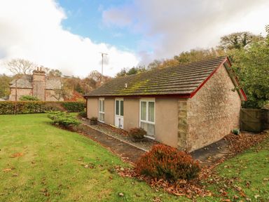 A small stone and stucco house with moss on the roof surrounded by grass and bushes at Old School Muncaster House Ravenglass near Holmrook