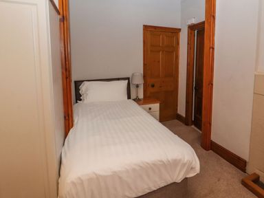 A small bedroom with a single bed a bedside table with a lamp two wooden doors and carpeted floor at Old School Muncaster House Ravenglass near Holmrook