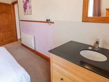 A bedroom corner with a wooden door heater and sink unit at Old School Muncaster House Ravenglass near Holmrook