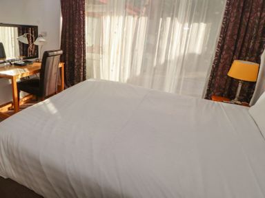 A bedroom with a large bed next to a desk with a chair and a lamp and curtains on windows at Old School Muncaster House Ravenglass near Holmrook