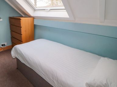 A bedroom with a single bed a white pillow a wooden chest of drawers and a skylight window at Old School Muncaster House Ravenglass near Holmrook