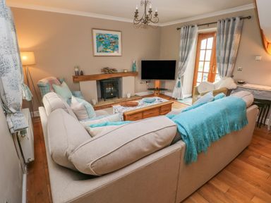 A living room with beige sofas a wooden coffee table a fireplace and a television at North Studdock Cottage in Angle near Pembroke