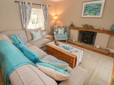 A living room with a beige sectional sofa with blue pillows a wooden coffee table and a fireplace at North Studdock Cottage in Angle near Pembroke