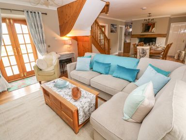 A living room with two sofas and an armchair near wooden stairs and a dining table at North Studdock Cottage in Angle near Pembroke