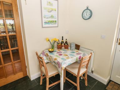 A small dining area with a table covered by a patterned tablecloth and three wooden chairs at North Studdock Cottage in Angle near Pembroke