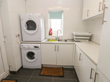 A laundry room with a stacked washer and dryer a sink with a window above and white cabinets at North Studdock Cottage Angle near Pembroke