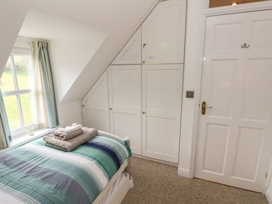 A bedroom with a single bed with folded towels a window with curtains built in wardrobes and a door at North Studdock Cottage Angle near Pembroke