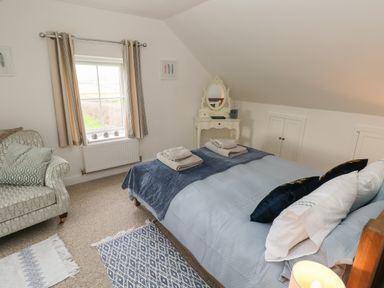 A bedroom with a bed folded towels a patterned armchair a dressing table and rugs at North Studdock Cottage in Angle near Pembroke