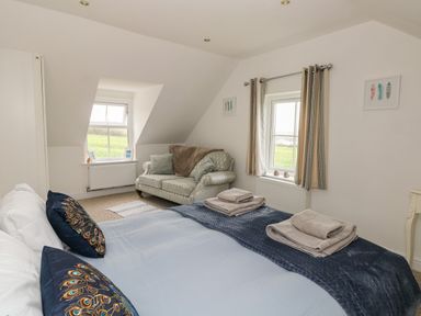 A bedroom with a bed with folded towels two windows with curtains a patterned sofa and framed pictures on the wall at North Studdock Cottage in Angle near Pembroke
