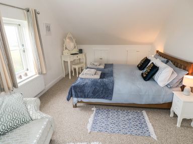 A bedroom with a double bed a vanity table a chair a window with curtains and a patterned rug on the floor at North Studdock Cottage in Angle near Pembroke