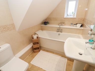A bathroom with a bathtub, sink, toilet, small window, and storage basket at North Studdock Cottage in Angle near Pembroke