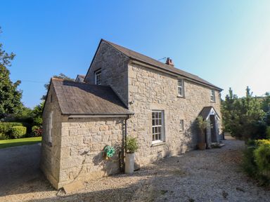 A stone house with a pitched roof and gravel driveway surrounded by plants at Lower Gadles in Burnthouse near Falmouth