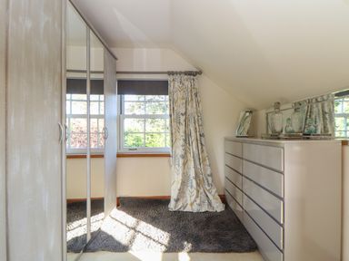 A dressing room with a wardrobe, a window with curtains, a chest of drawers, and a rug at Lower Gadles Burnthouse near Falmouth