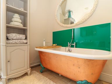 A bathroom with a copper bathtub green backsplash a white cabinet with towels and a round mirror at Lower Gadles Burnthouse near Falmouth