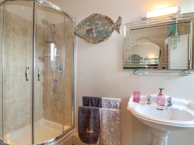 A bathroom with a corner shower, a sink with soap dispenser, a mirror, and towels on a towel rack at Lower Gadles in Burnthouse near Falmouth