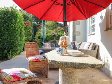 An outdoor patio with wicker chairs and a stone table under a red umbrella at Lower Gadles in Burnthouse near Falmouth