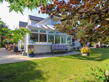 A garden with a bench with cushions and a conservatory attached to a house at Lower Gadles Burnthouse near Falmouth